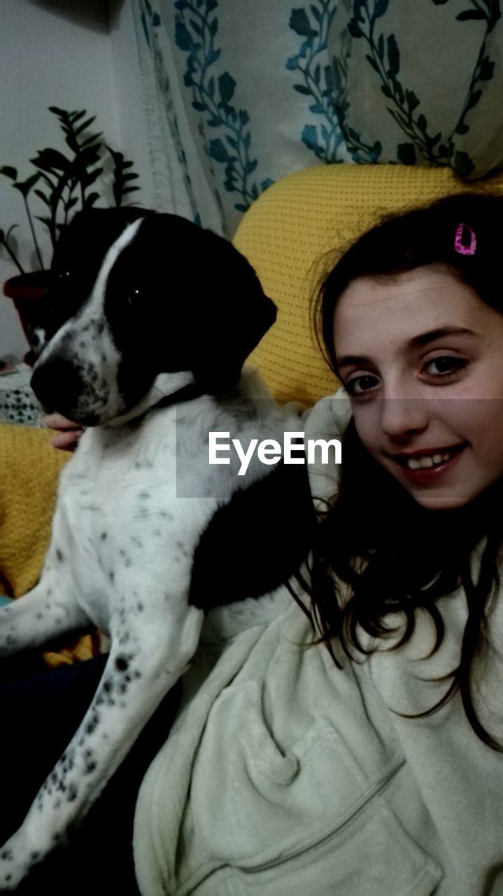 CLOSE-UP PORTRAIT OF YOUNG WOMAN WITH DOG AT HOME