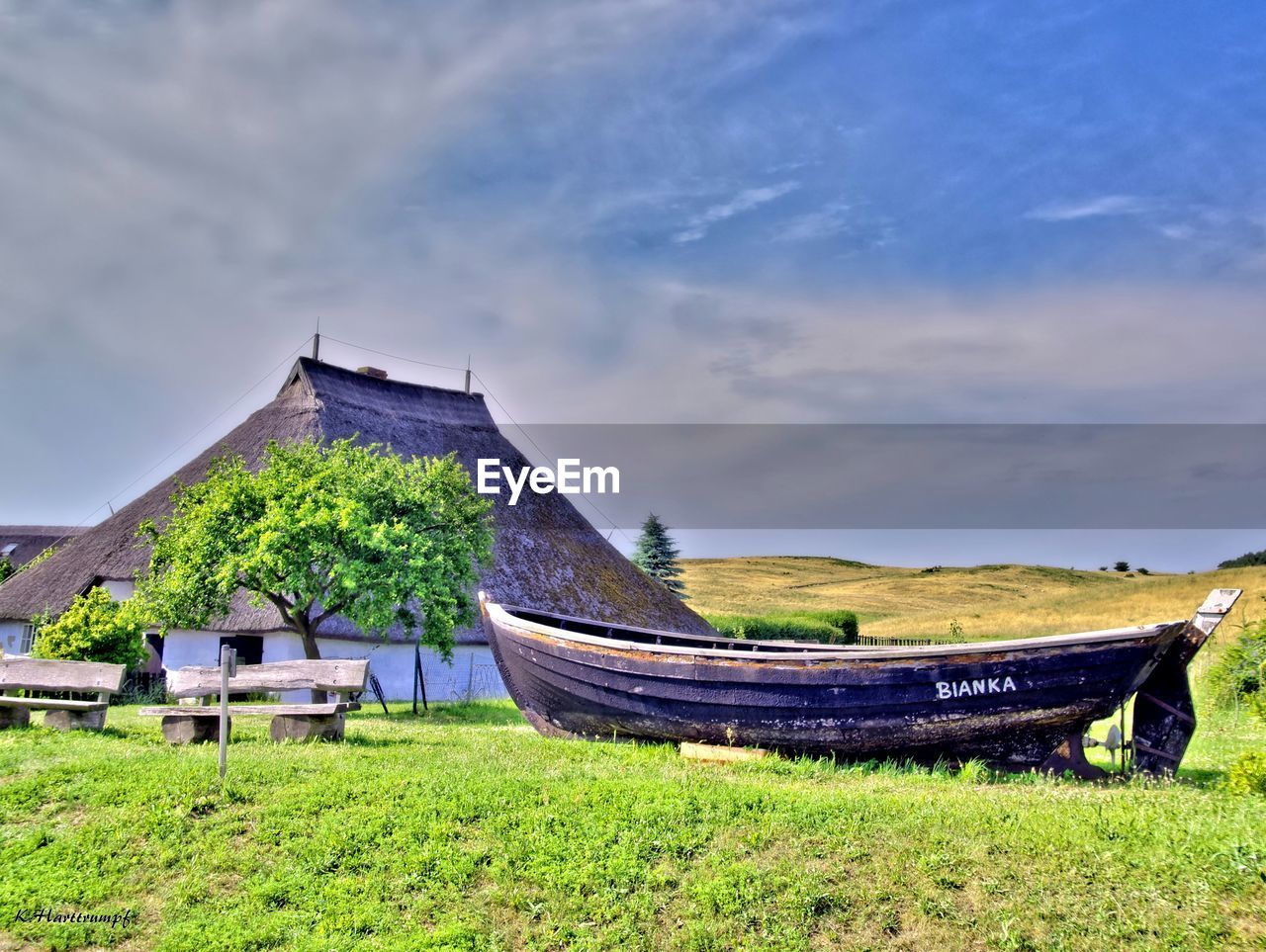 Boat moored on grassy field by house against cloudy sky