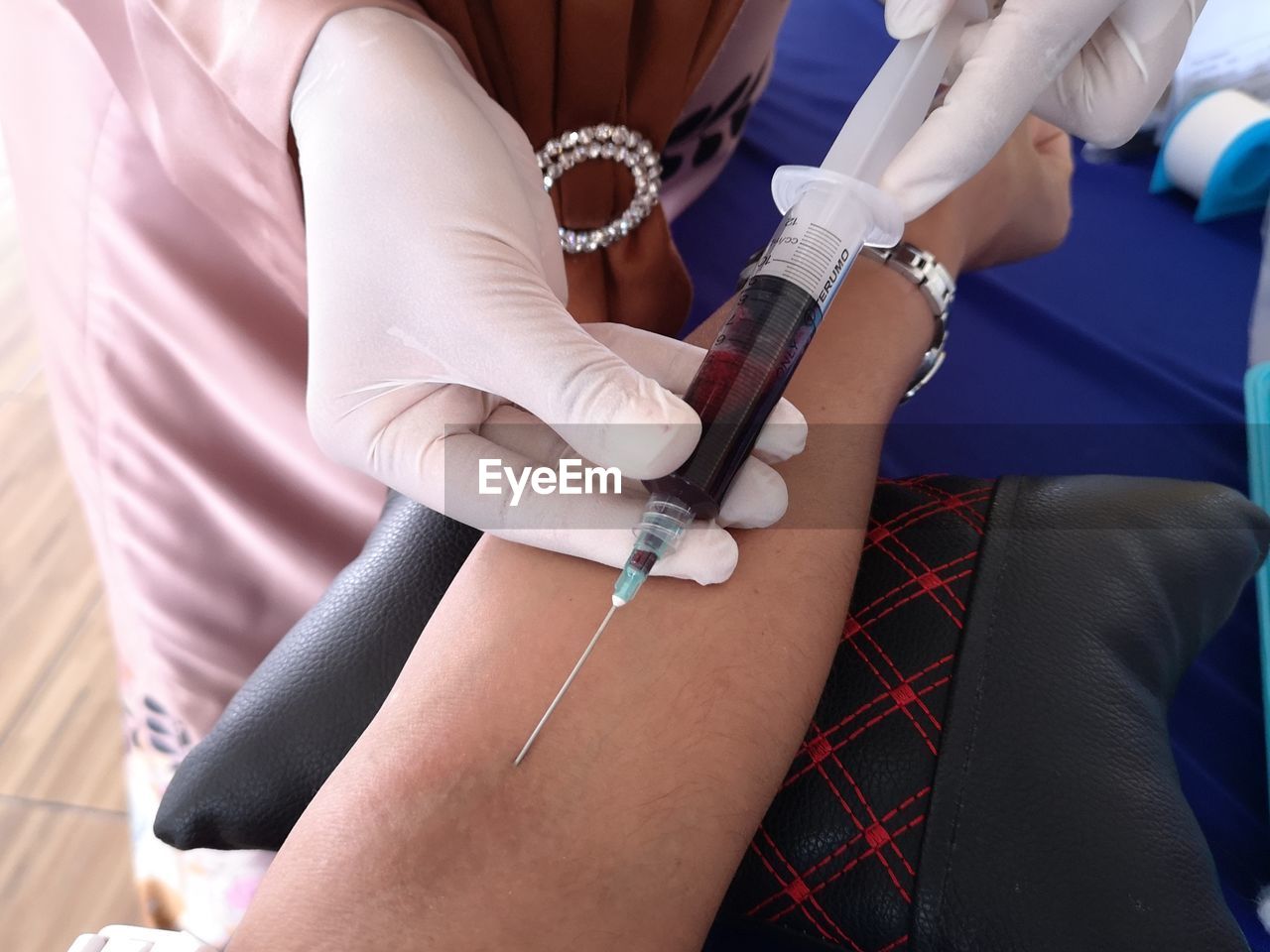 Midsection of doctor removing blood through injection in clinic