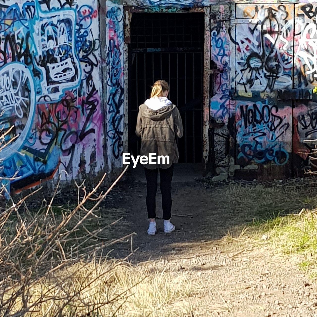 REAR VIEW OF WOMAN STANDING AGAINST GRAFFITI ON WALL