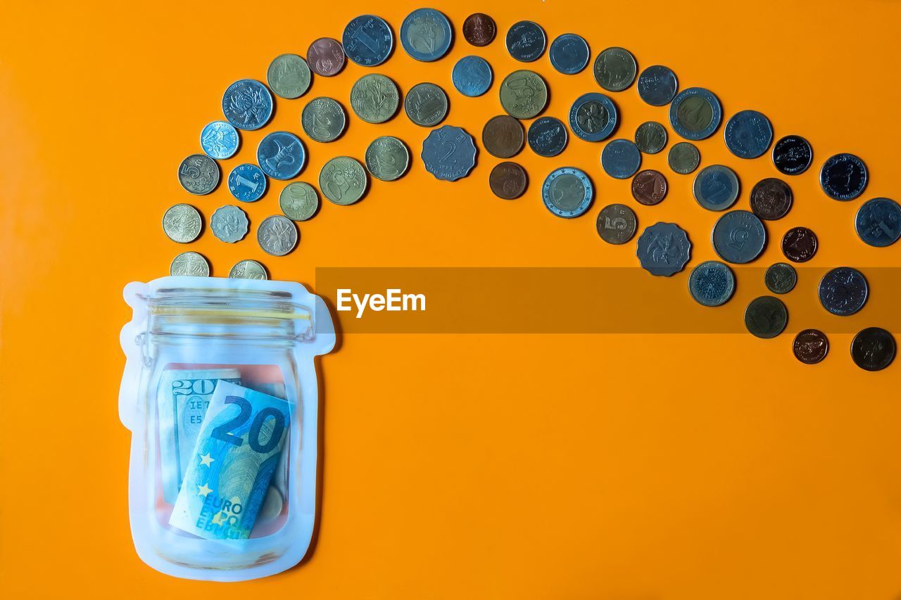 Close-up of coins spilling from jar against orange background