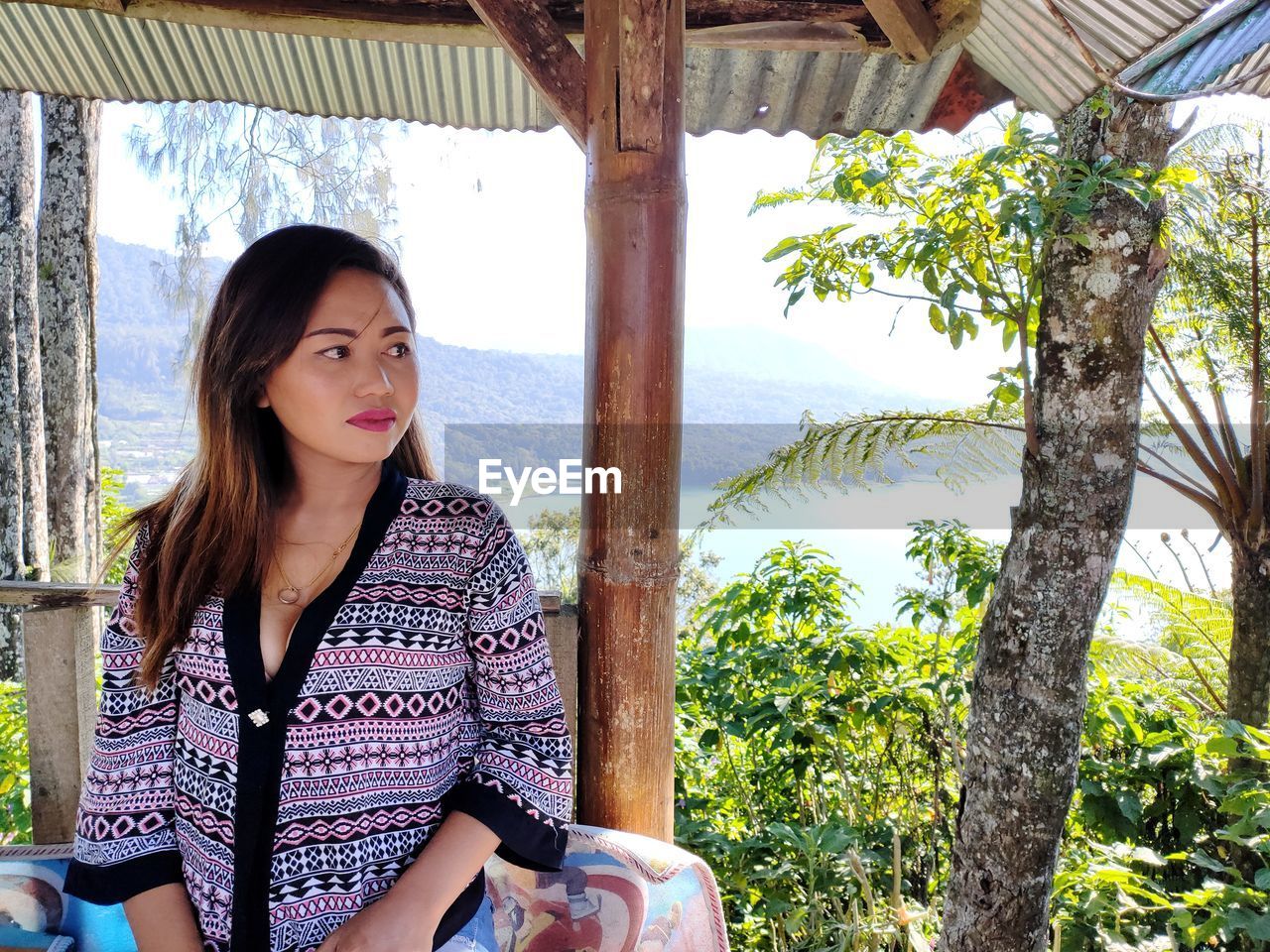 PORTRAIT OF BEAUTIFUL YOUNG WOMAN STANDING BY TREE TRUNK