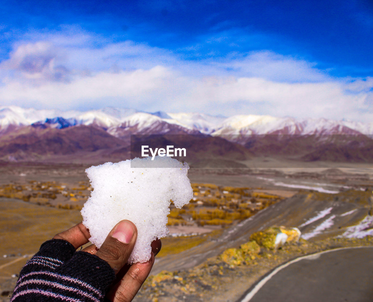 Cropped hand of person holding ice against mountain 