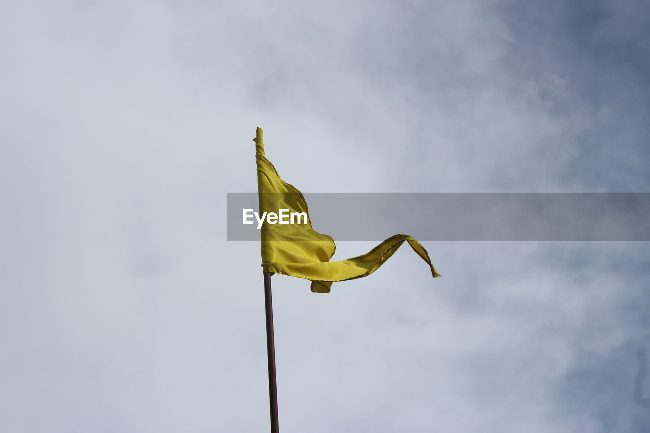Low angle view of yellow flag against sky