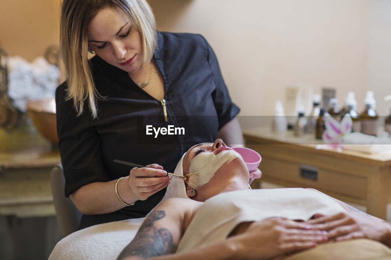 Beautician applying face mask to woman in spa