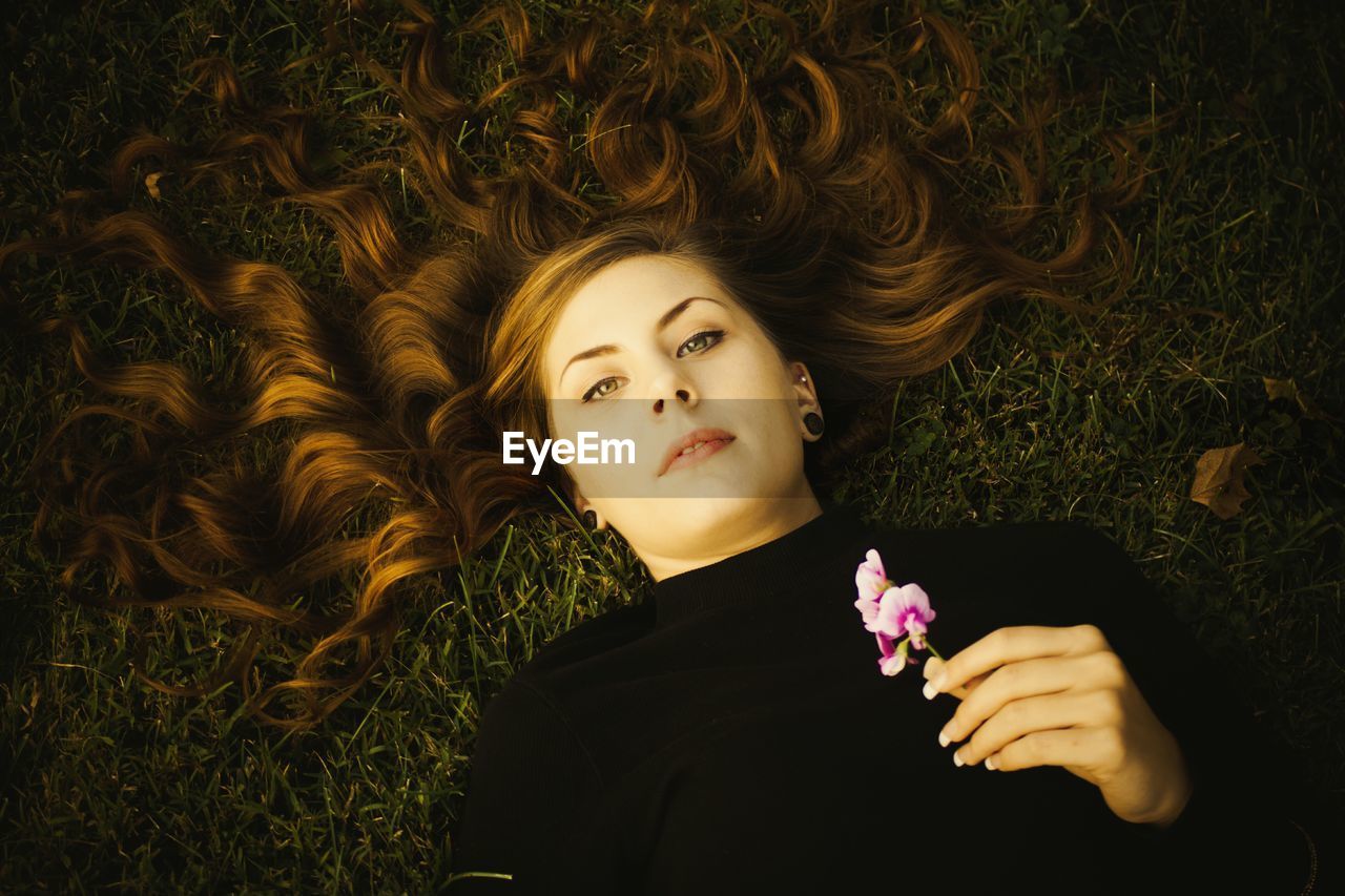 High angle portrait of holding flowers while lying on grassy field