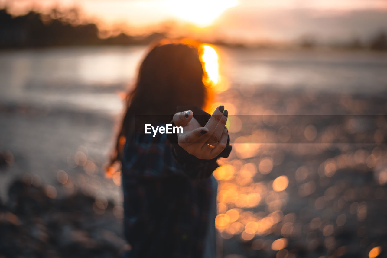 YOUNG WOMAN HOLDING CAMERA AT BEACH DURING SUNSET