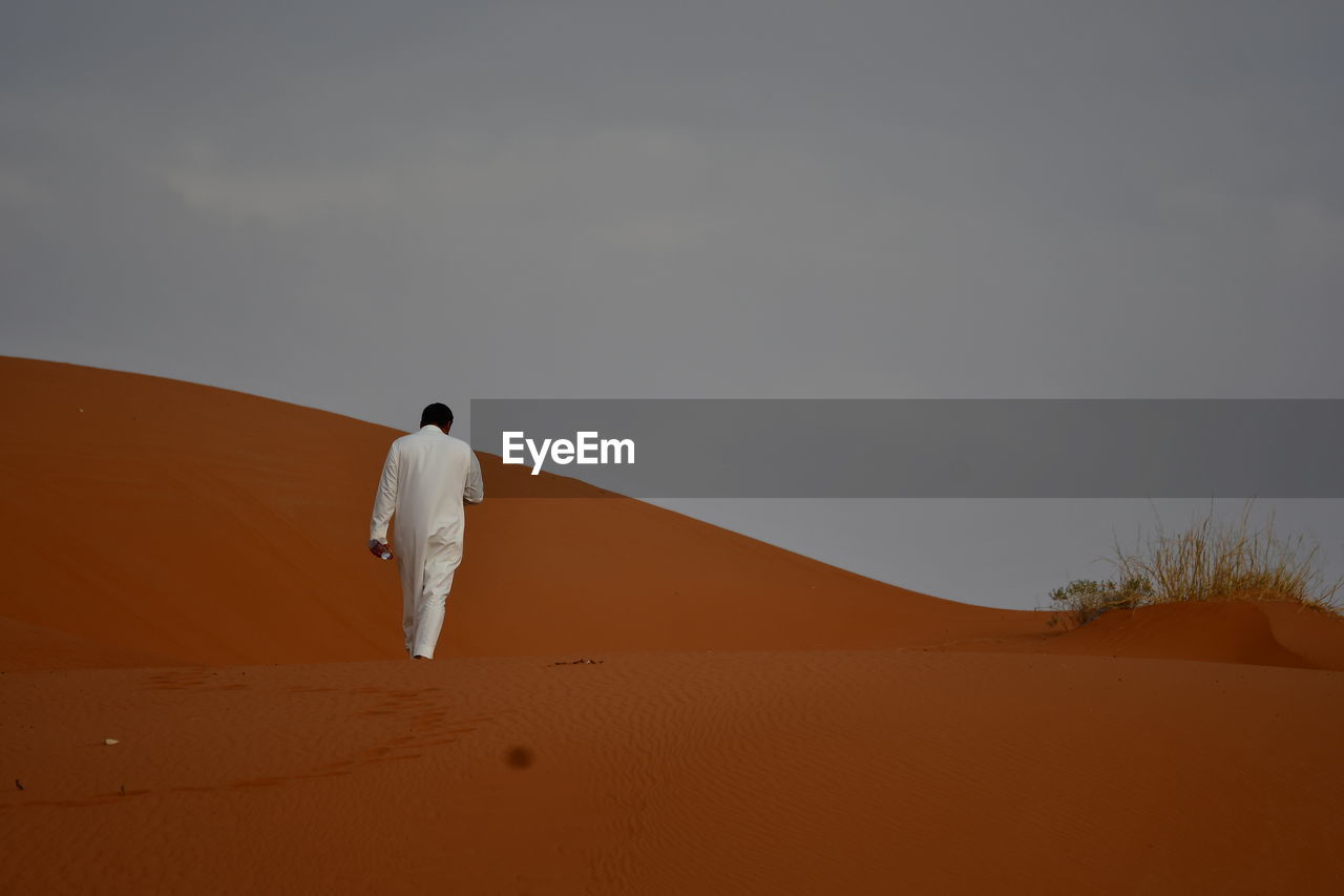 REAR VIEW OF MAN WALKING IN DESERT