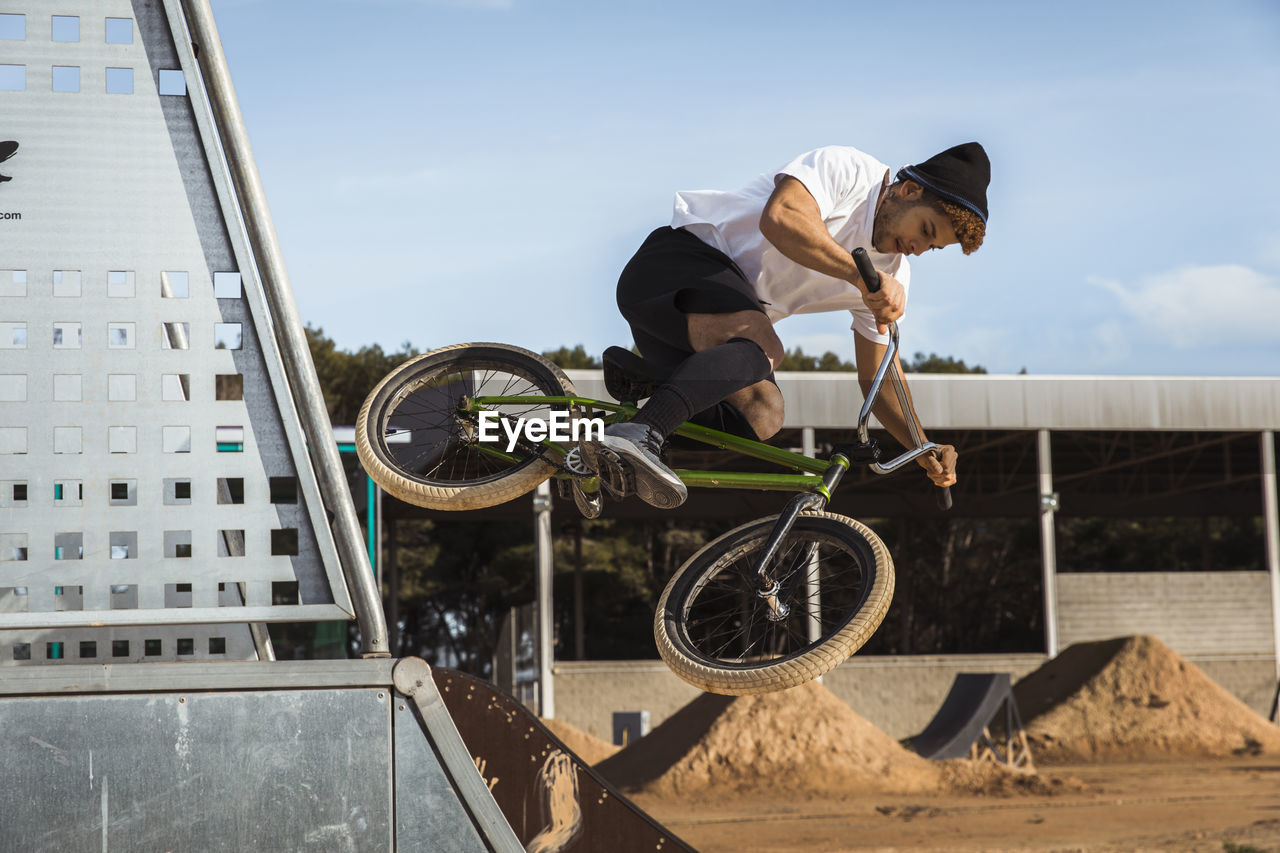 Young man jumping with bicycle at bike park on sunny day