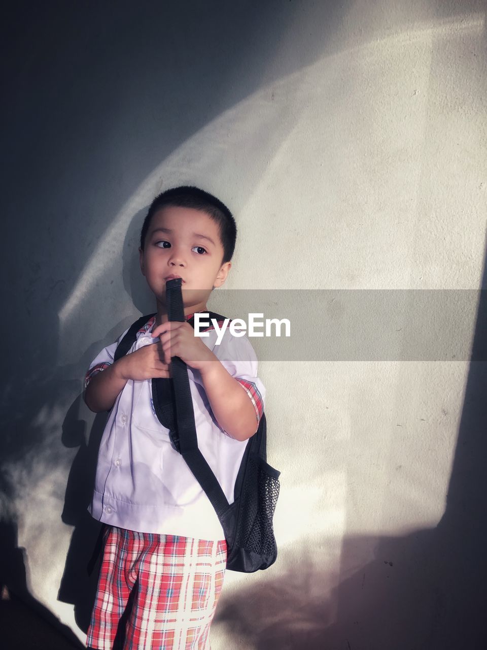 Cute thoughtful schoolboy standing against wall