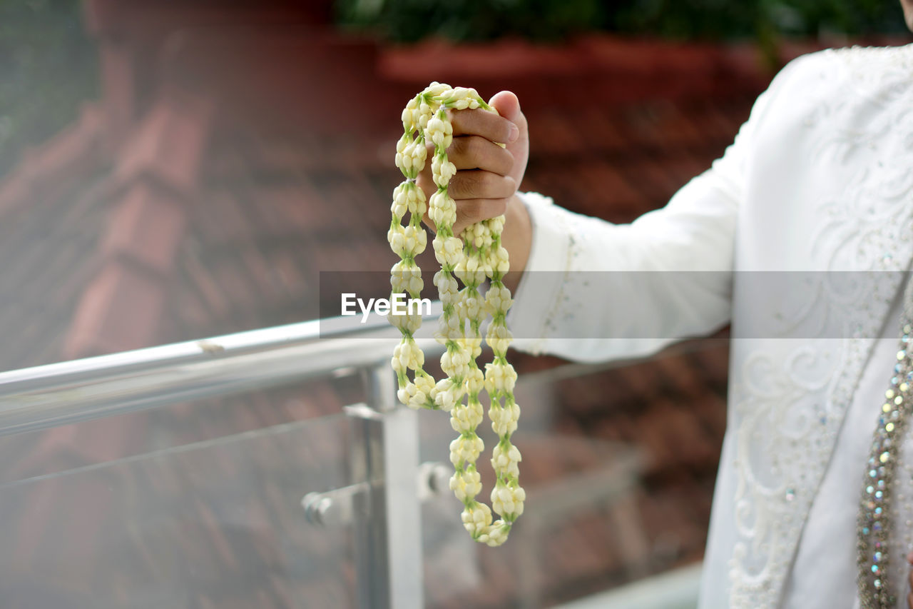 Midsection of groom holding jasmine necklace