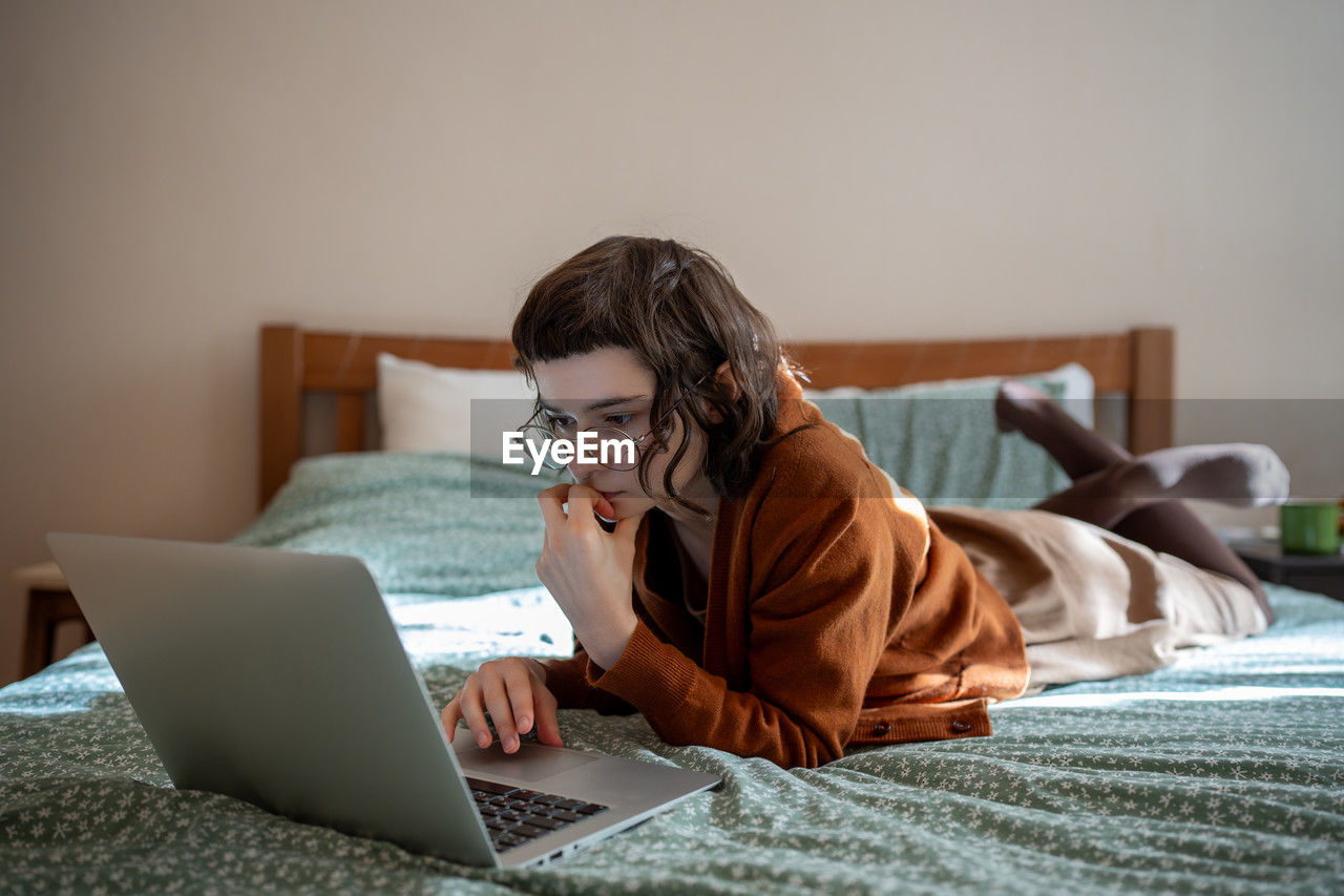 Concentrated teen girl reading book online, scrolling social networks in internet on laptop computer