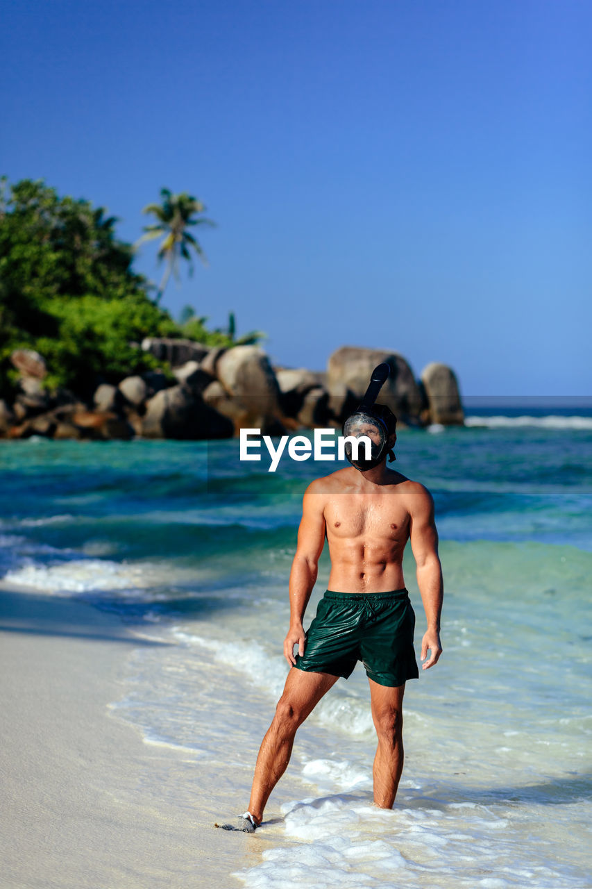 Shirtless man standing on shore at beach