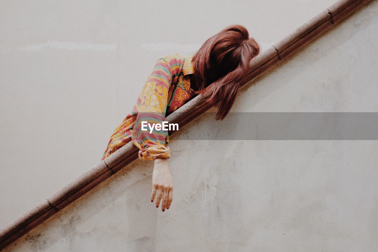 Low angle view of woman leaning on railing against white wall