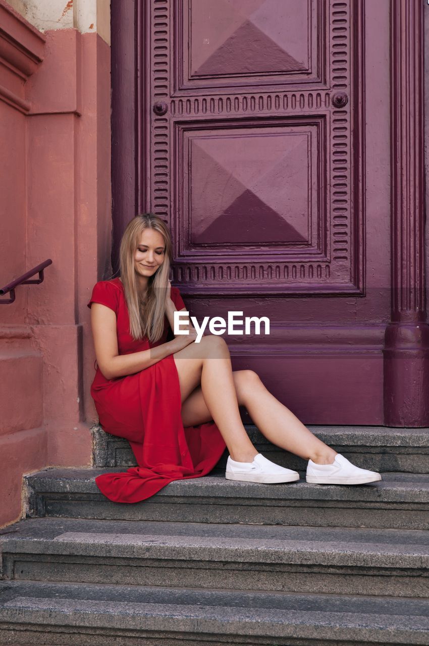 Full length of woman sitting on steps against closed doors