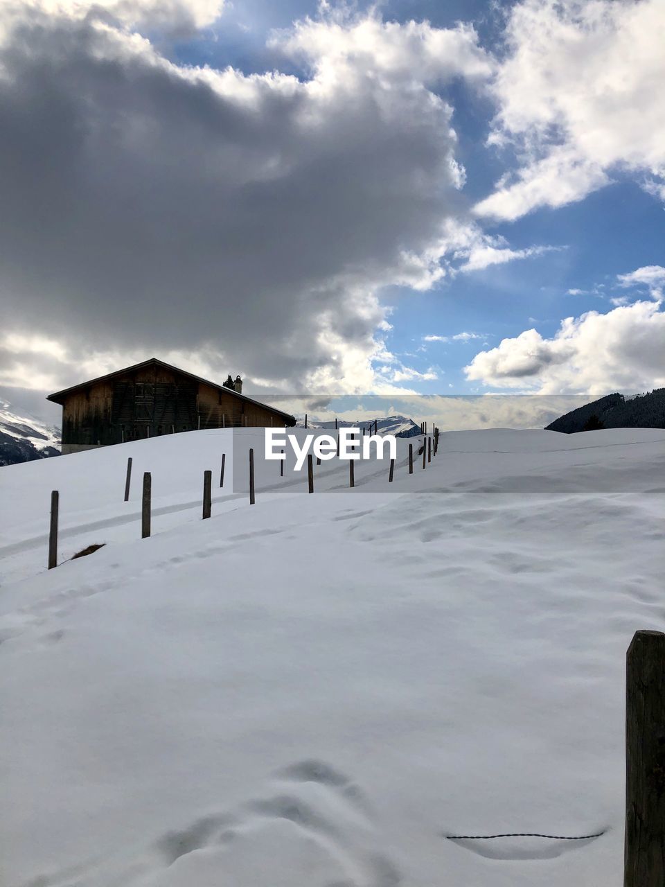 WOODEN POST ON SNOW COVERED LAND AGAINST SKY