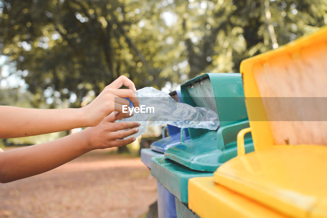 Cropped image of hands throwing crushed bottles in recycling bin