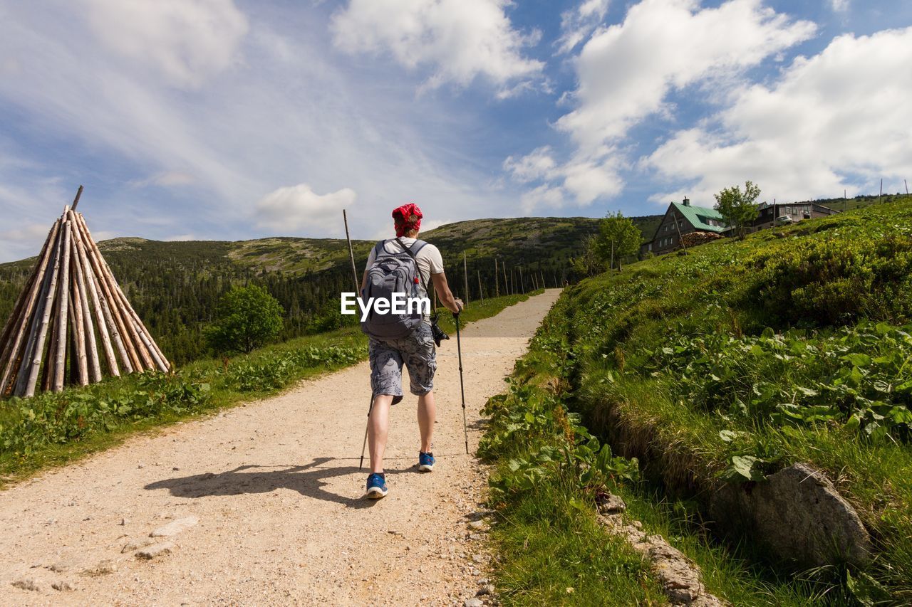 Rear view of hiker walking on footpath against cloudy sky