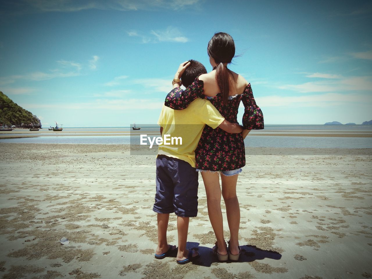 Rear view of mother and son standing at beach during sunny day