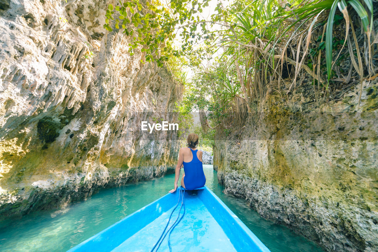 Rear view of woman in blue boat on river amidst rock formation