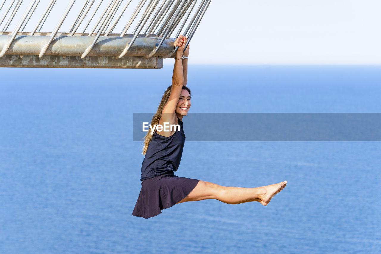 Happy mature woman hanging on railing while practicing acrobatics at viewpoint