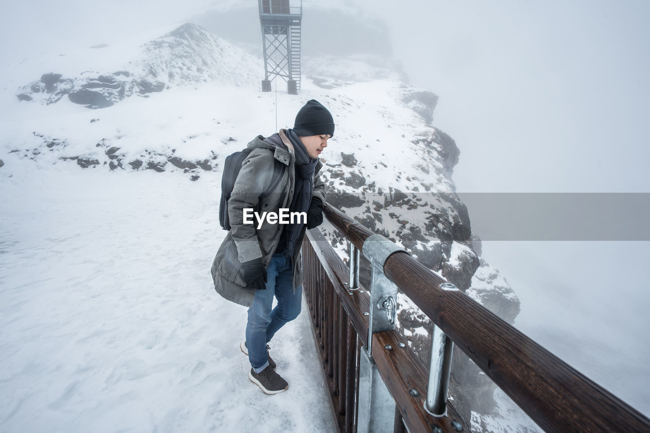Young man standing on snow covered mountain by railing