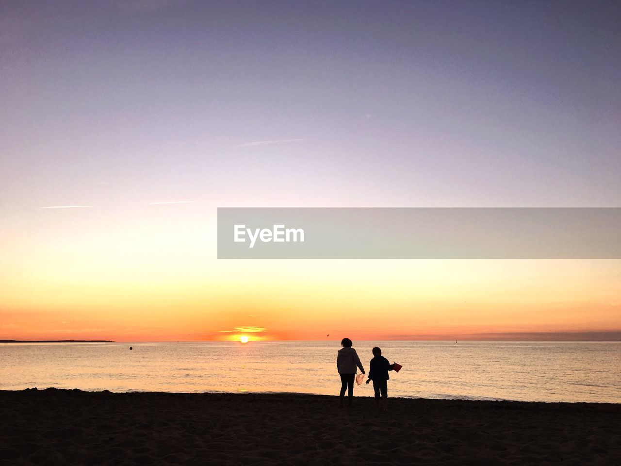 Silhouette people at beach against sky during sunset