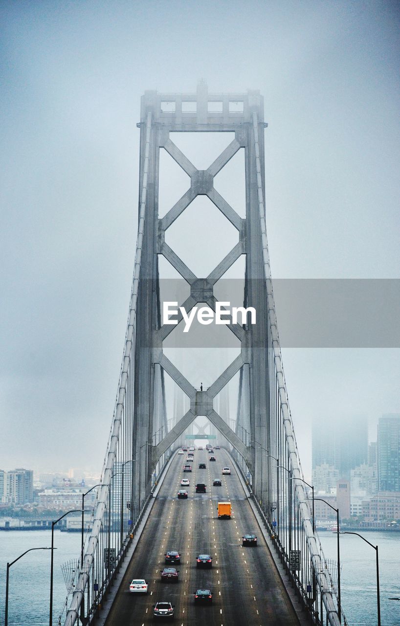 Cars on bridge over lake against sky in city