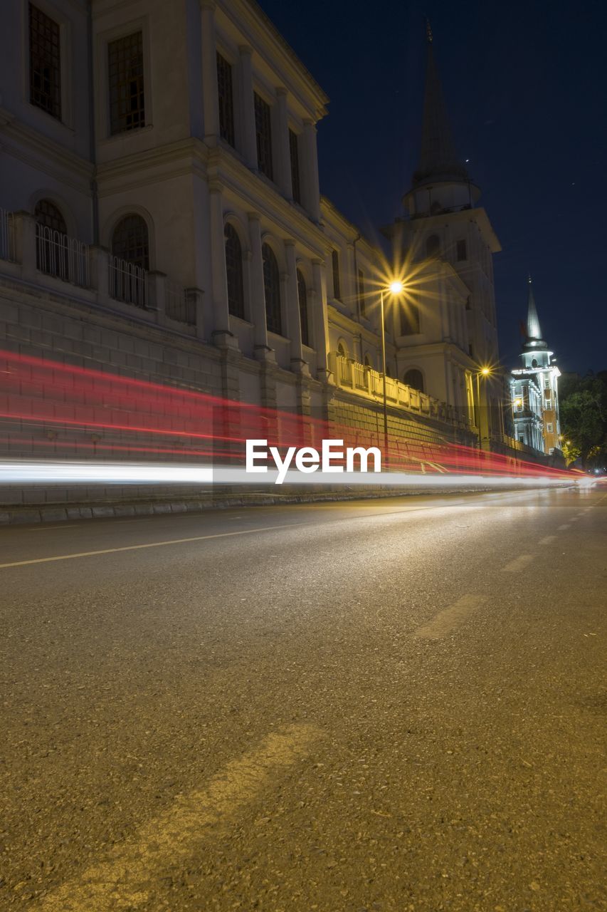 LIGHT TRAILS ON ROAD BY ILLUMINATED BUILDINGS AT NIGHT