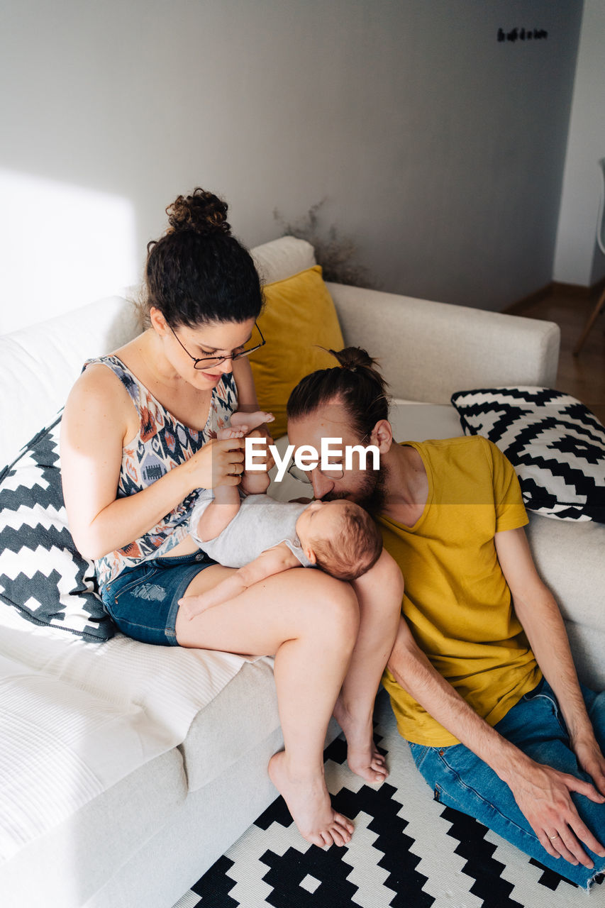 High angle view of young parents relaxing on bed at home kissing new born baby