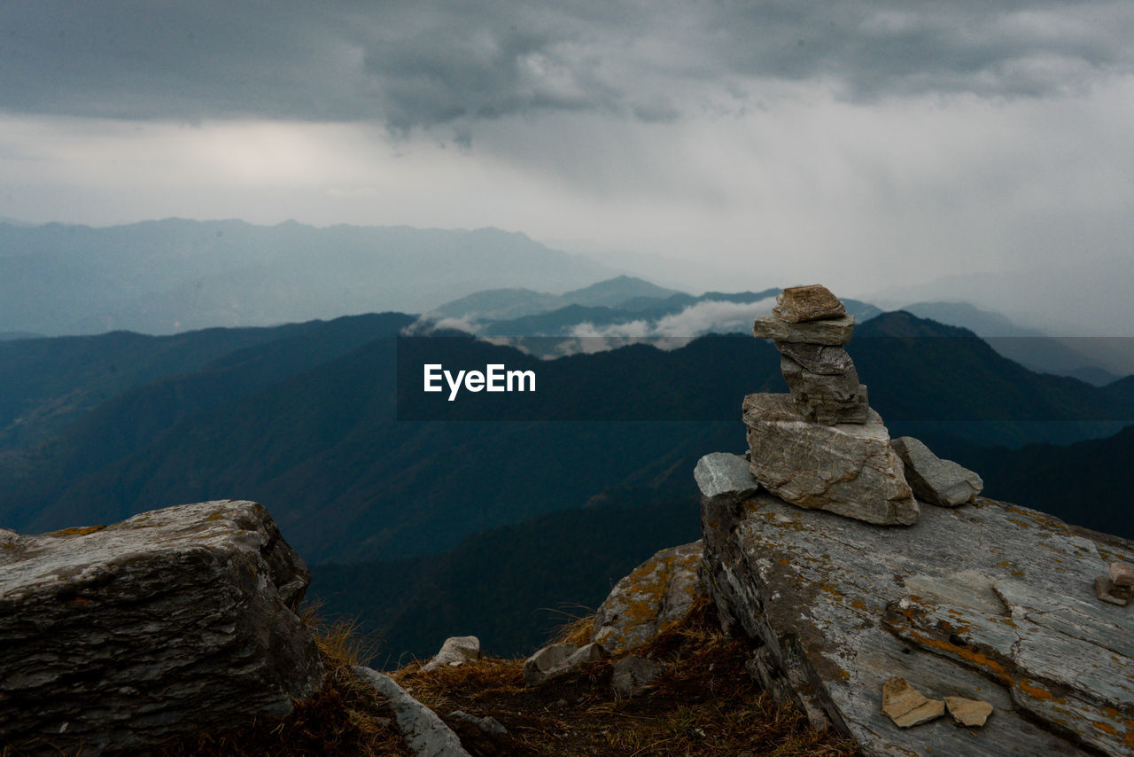 Stack of rocks on mountain against cloudy sky