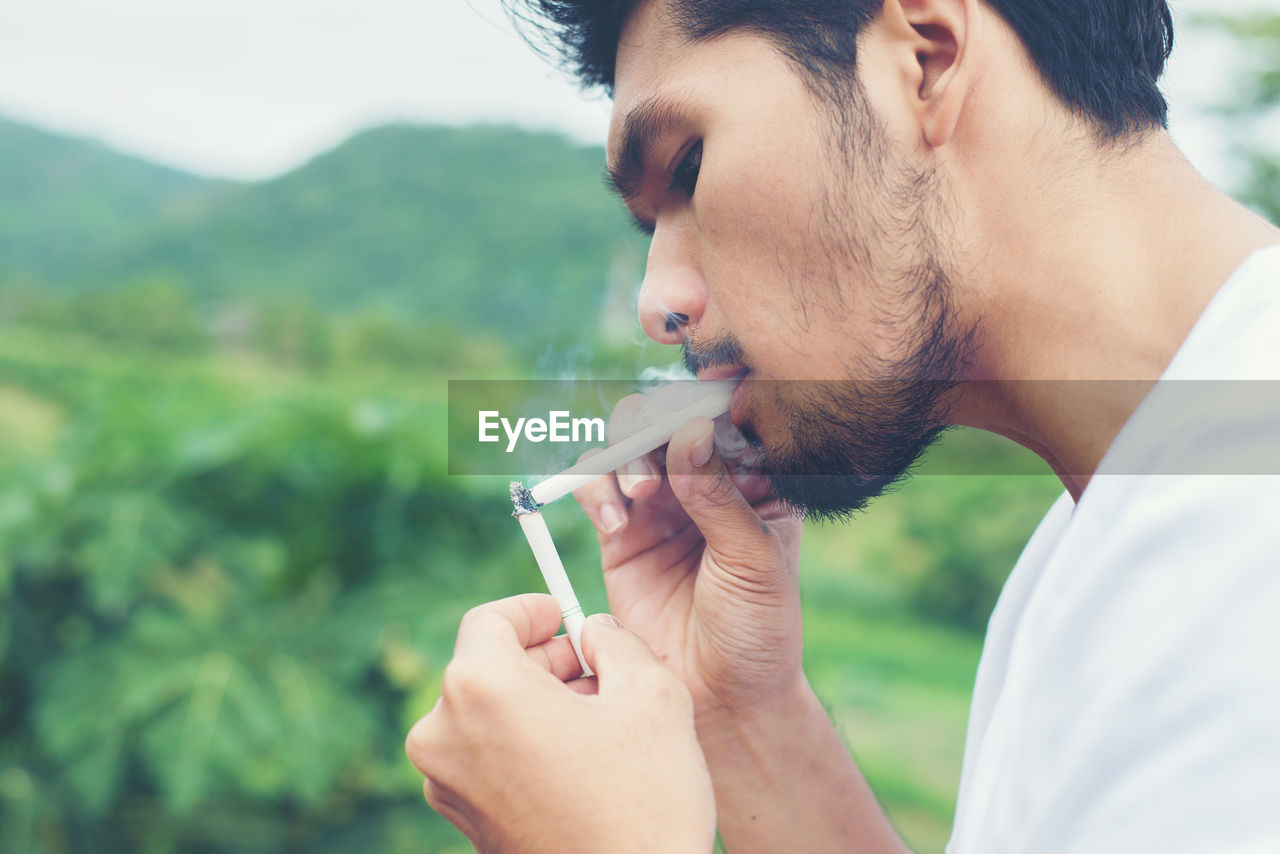 Man smoking cigarette against mountains