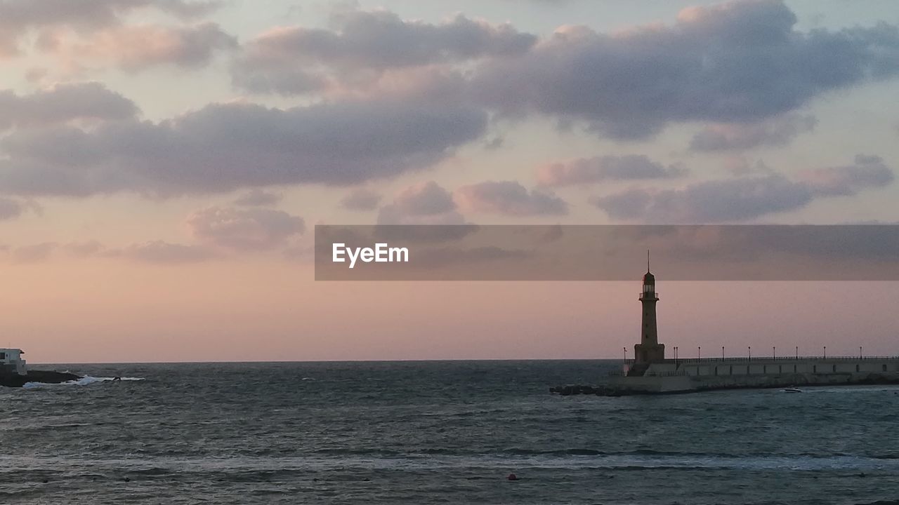 Lighthouse by sea against sky during sunset