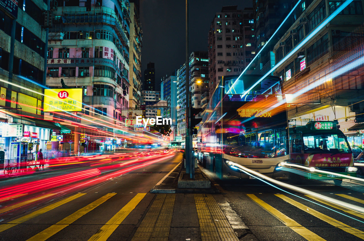 LIGHT TRAILS ON CITY STREET AMIDST BUILDINGS