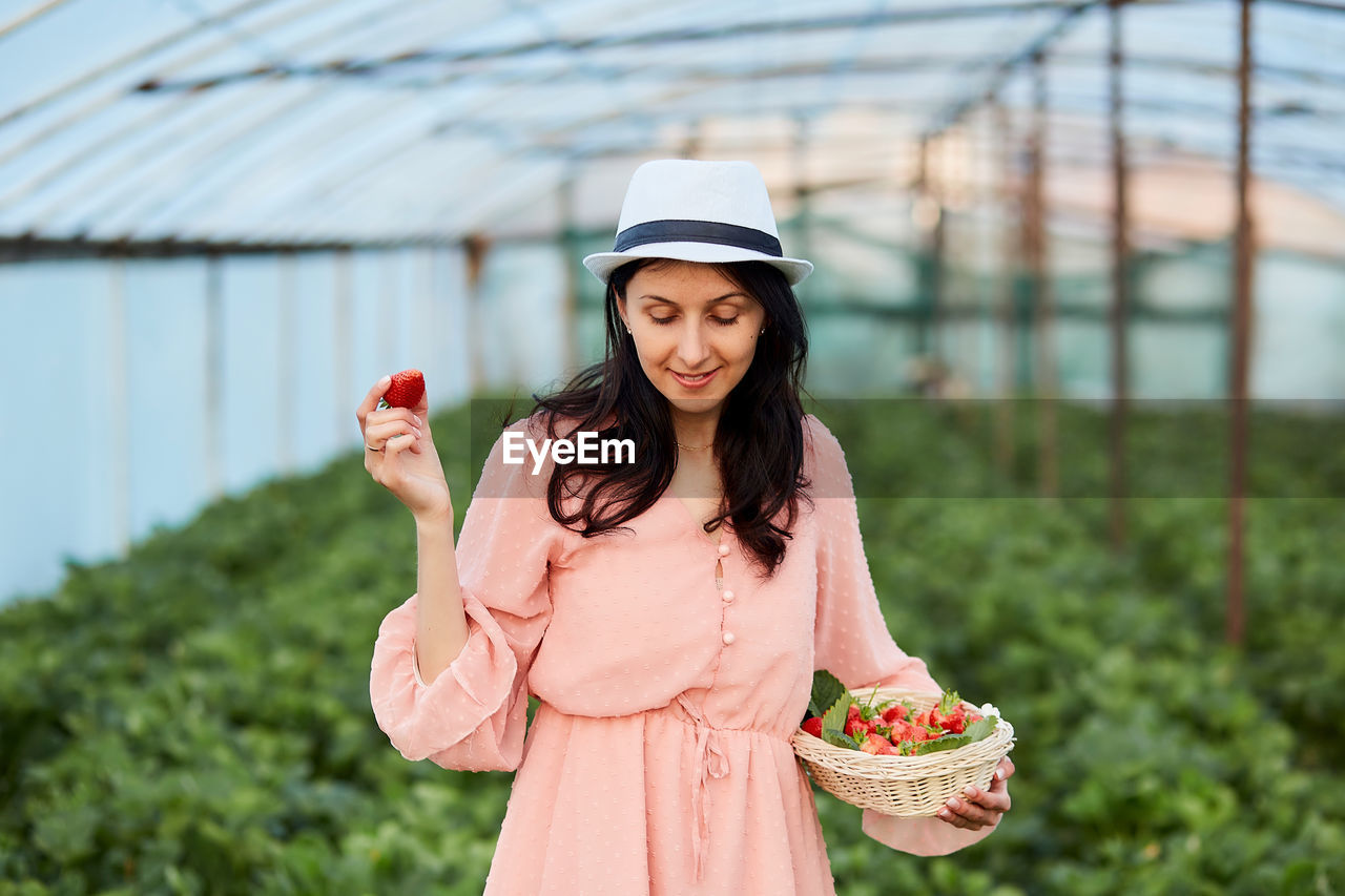 Smiling woman holding basket of strawberries at farm