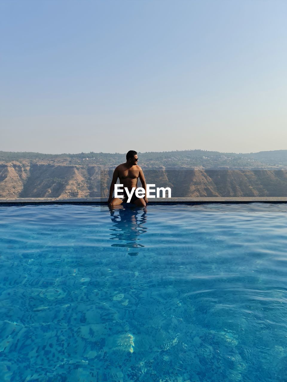 REAR VIEW OF SHIRTLESS MAN IN SWIMMING POOL AGAINST SKY