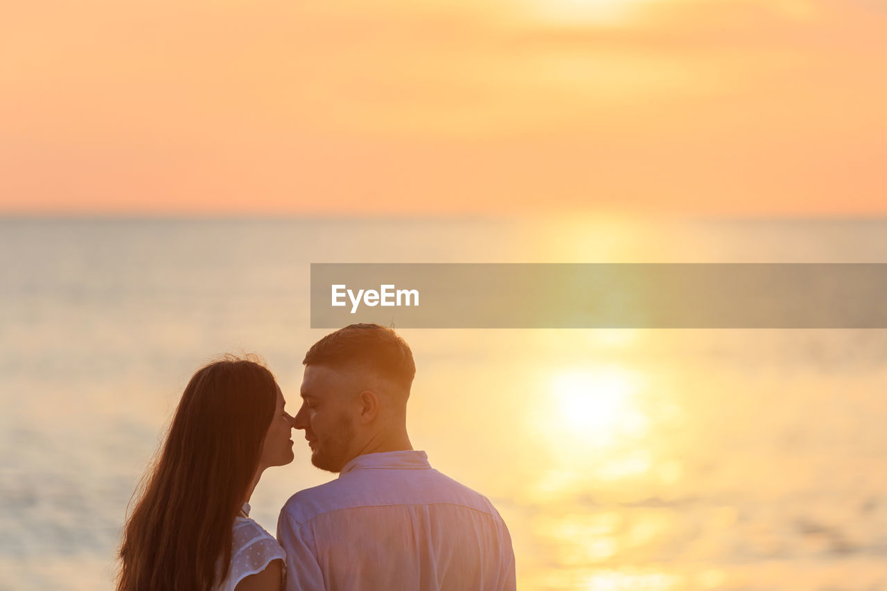 Couple romancing at beach against sky during sunset