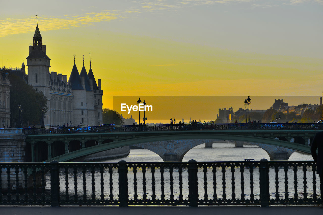 Bridge over river and buildings against sky during sunset