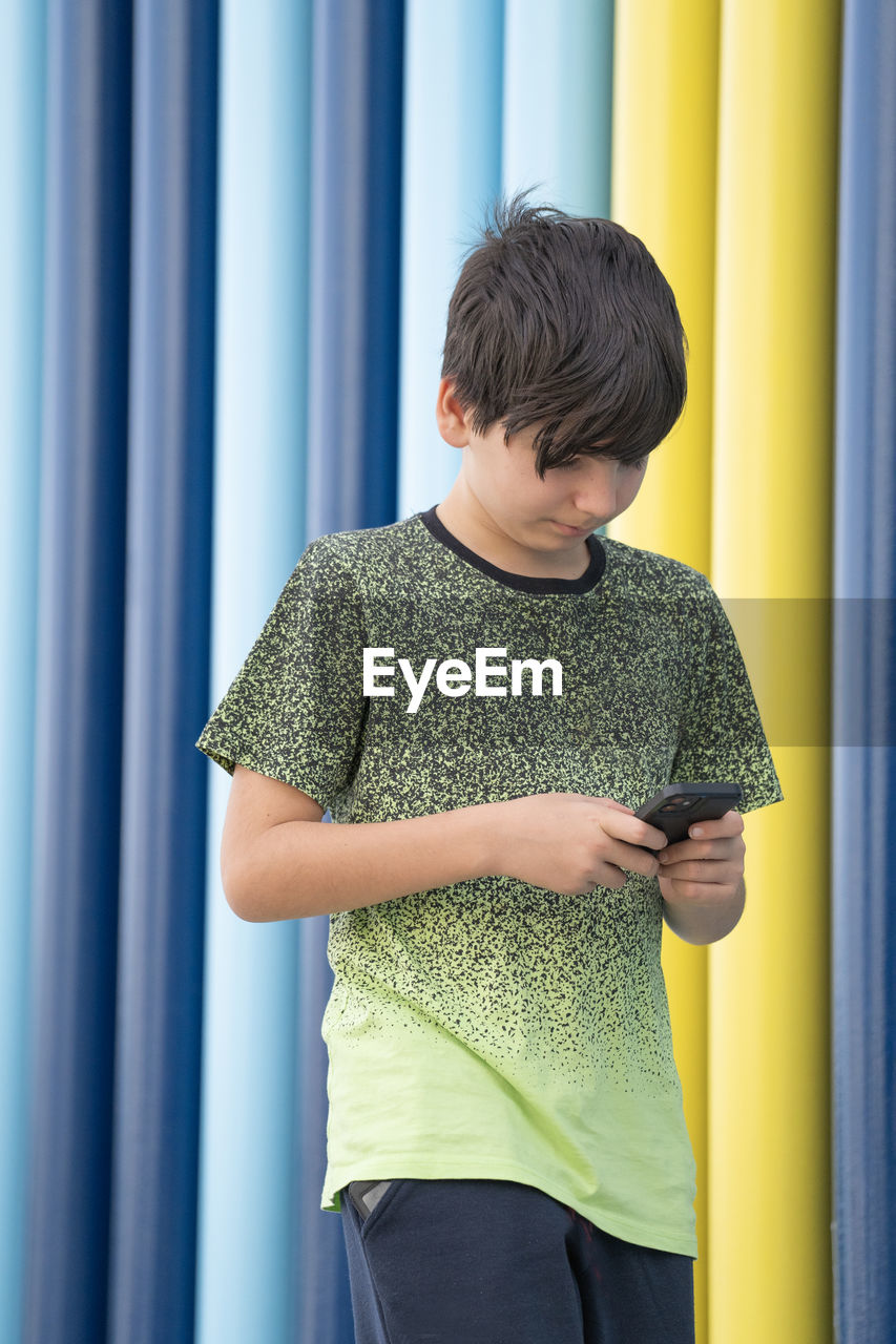 Portrait of a young boy using smartphone walking on coloured background. immersed technology concept