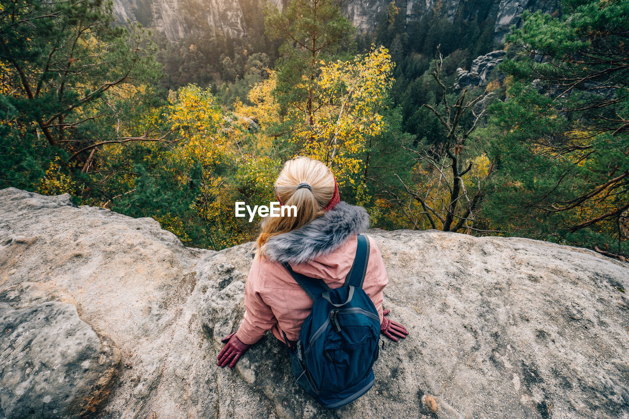 Rear view of woman sitting on rock while looking at view