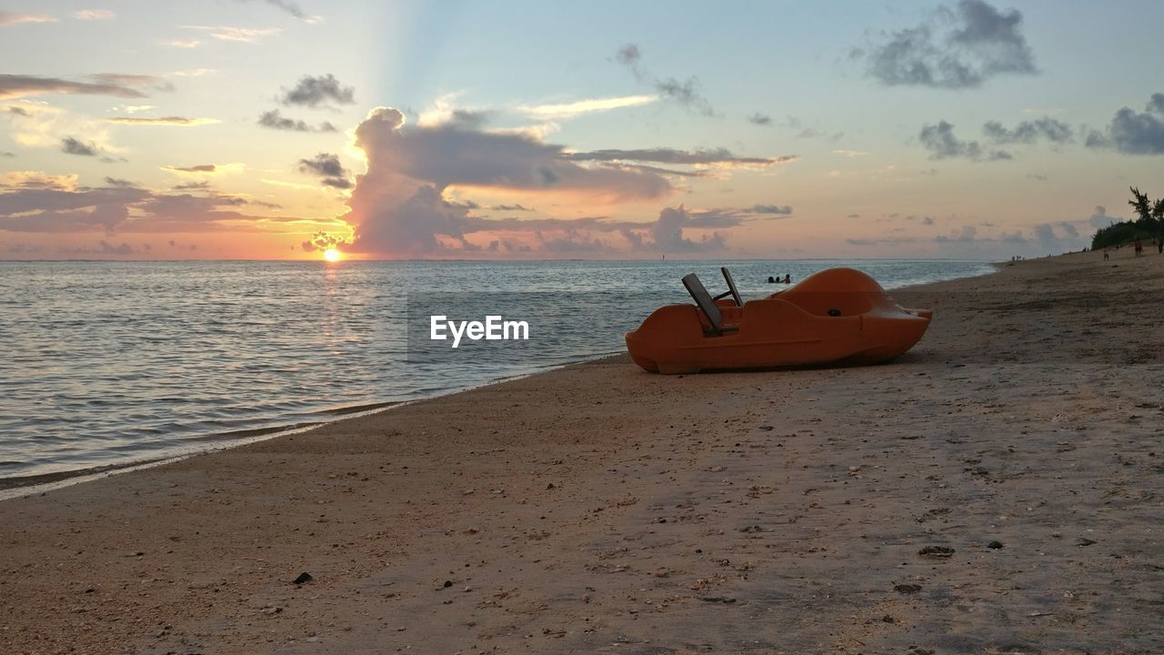 Boat moored on shore at beach against sky during sunset