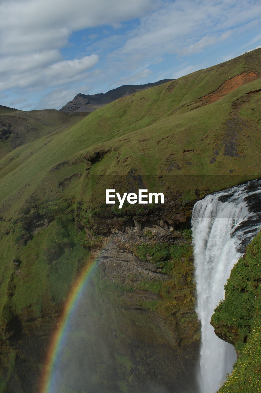 SCENIC VIEW OF WATERFALL BY MOUNTAINS AGAINST SKY