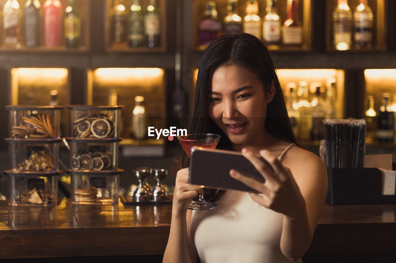 YOUNG WOMAN USING MOBILE PHONE IN BAR