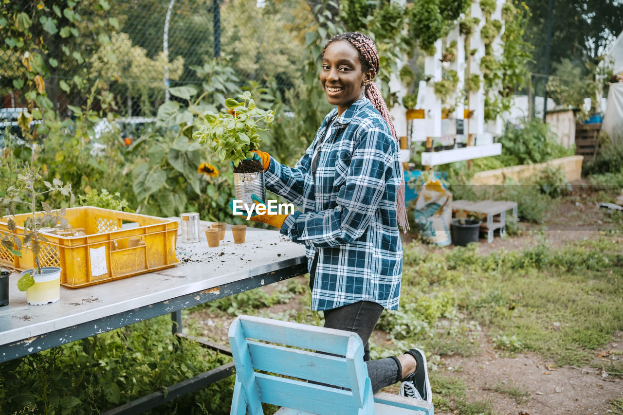 Portrait of smiling female farmer with potted plant in community garden
