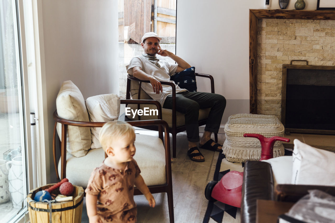 Father looking at toddler son while sitting on chair at home