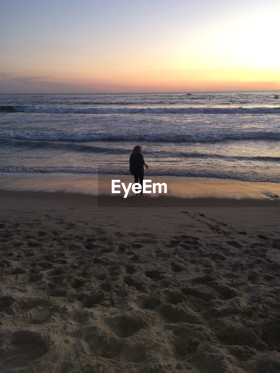 REAR VIEW OF SILHOUETTE WOMAN STANDING ON BEACH AGAINST SKY