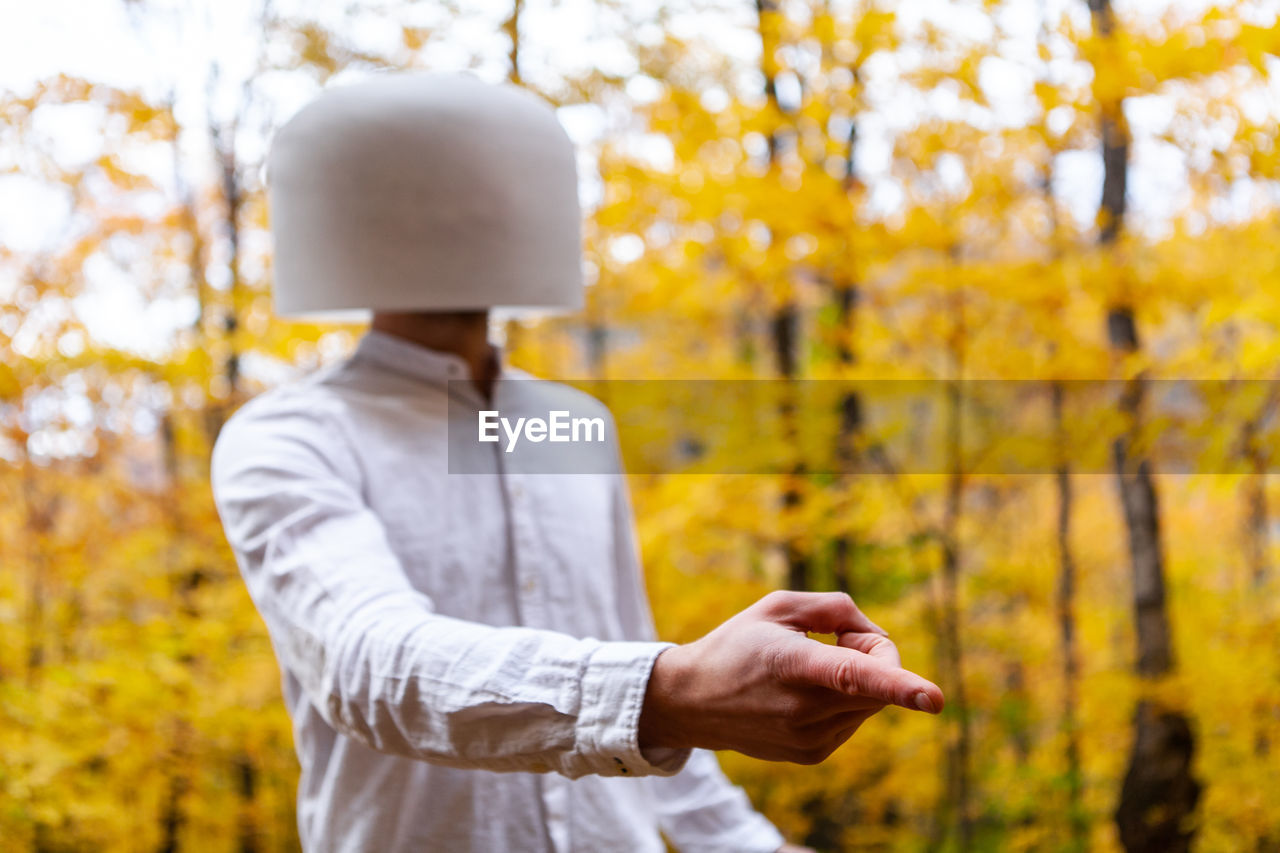 Man wearing bowl on head pointing away against trees