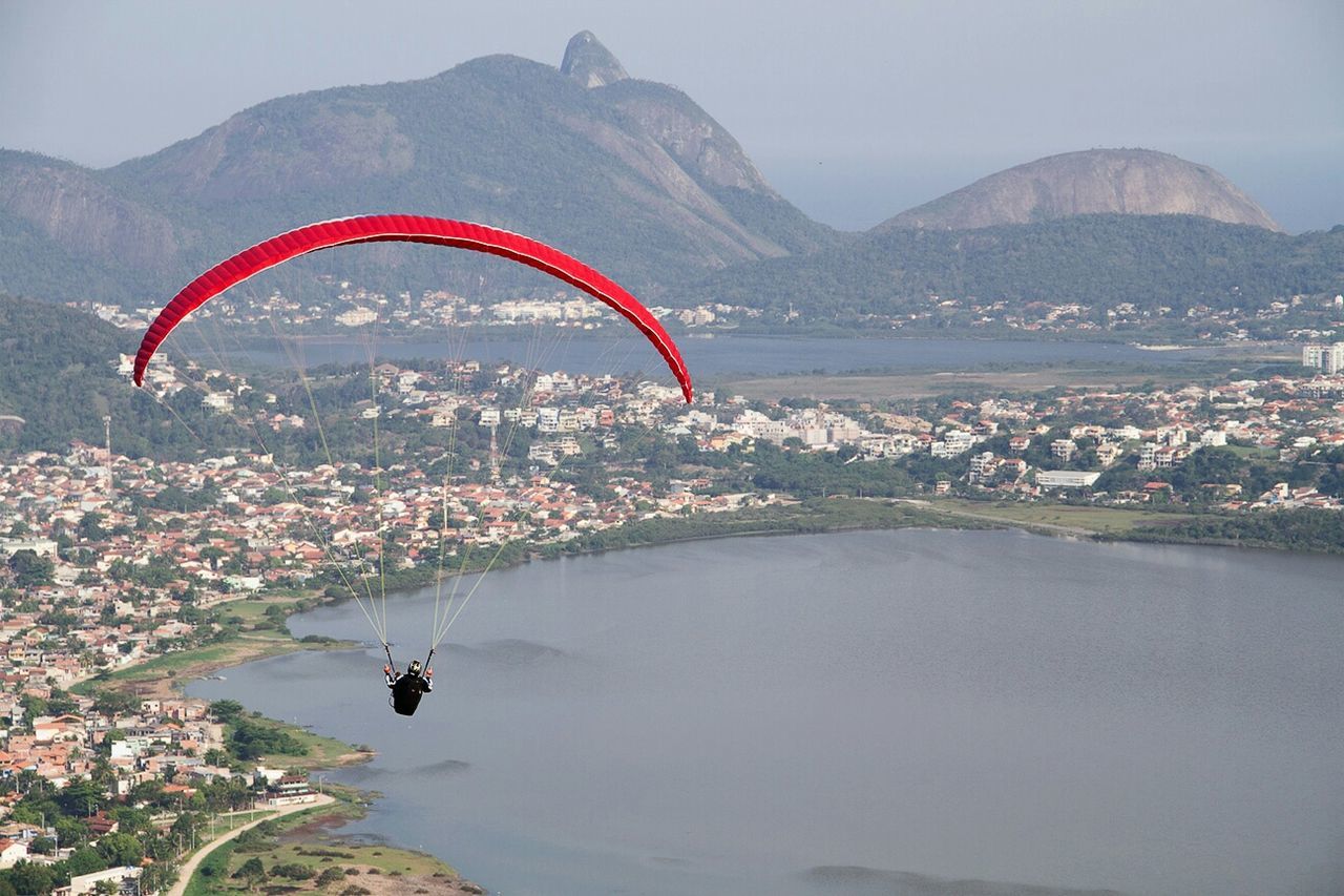 Person paragliding over lake in city
