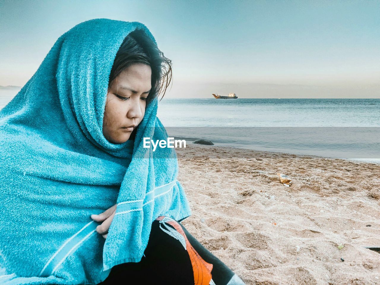 Woman wrapped in towel while sitting at beach