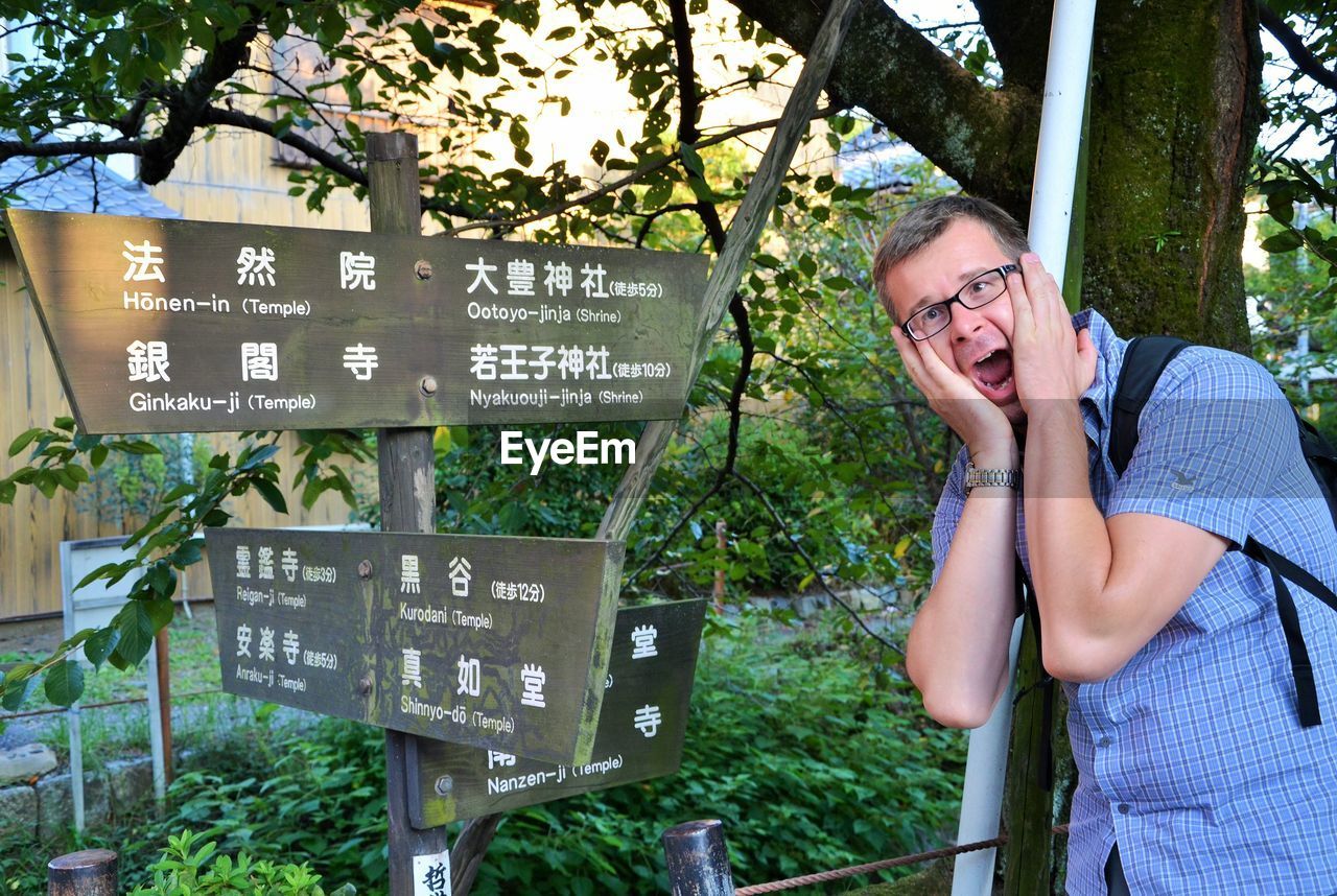 Portrait of surprised mid adult man standing by directional sign